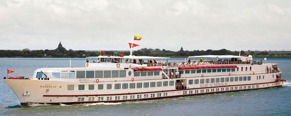 The Belmond Road to Mandalay luxury cruiser sailing past golden stupas on the riverbank